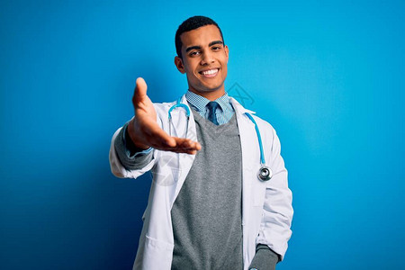 身穿大衣和听诊器的非洲帅哥医生在蓝色背景上微笑图片