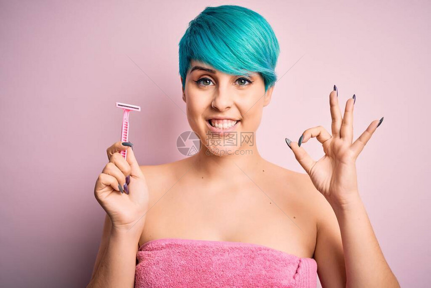 一头蓝色时尚头发头戴粉色毛巾拿着美容剃须刀的年轻女用手指做好手势图片