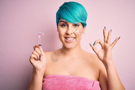 一头蓝色时尚头发头戴粉色毛巾拿着美容剃须刀的年轻女用手指做好手势图片