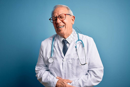 头发灰白的高级医生戴着听诊器和蓝色背景的医用外套图片