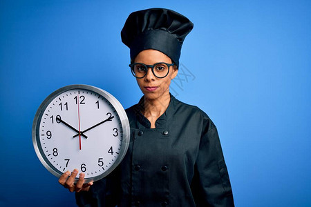 身穿厨师制服的非洲美面包师妇女戴帽子用时钟倒数自信地表现在图片