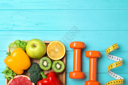 水果蔬菜测量胶带和轻蓝木制背景的哑铃图片
