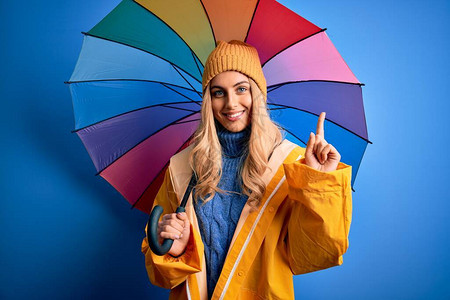 年轻漂亮的金发女郎穿着雨衣在雨天拿着五颜六色的雨伞图片