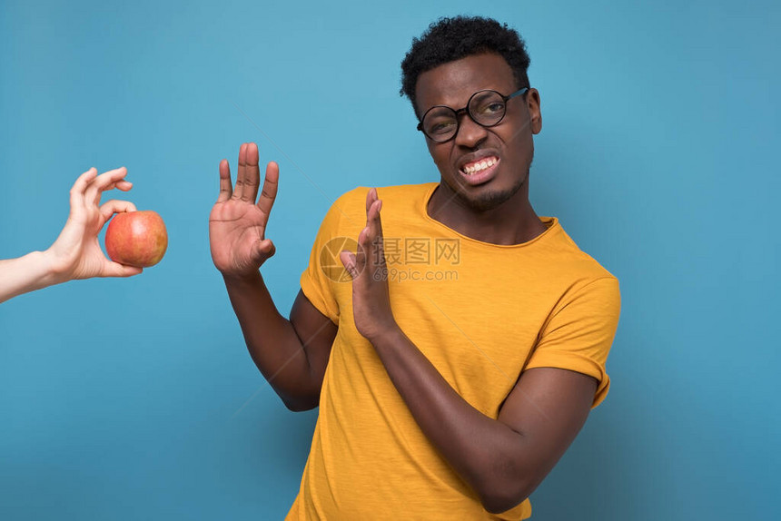 非洲黑人年轻男子拒绝吃蓝底孤立的苹果图片