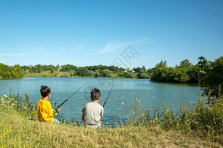两个男孩坐在池塘边钓鱼他们被美丽的大自然所包围钓鱼是图片