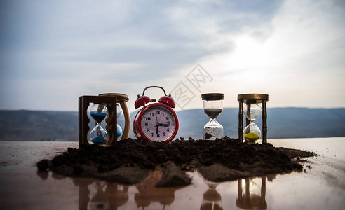 日落时有沙漏和红色闹钟时间概念图片