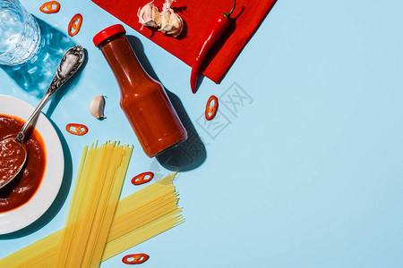 在蓝色背景的意大利面旁边放着大蒜和辣椒的辣番茄酱的顶部视图图片