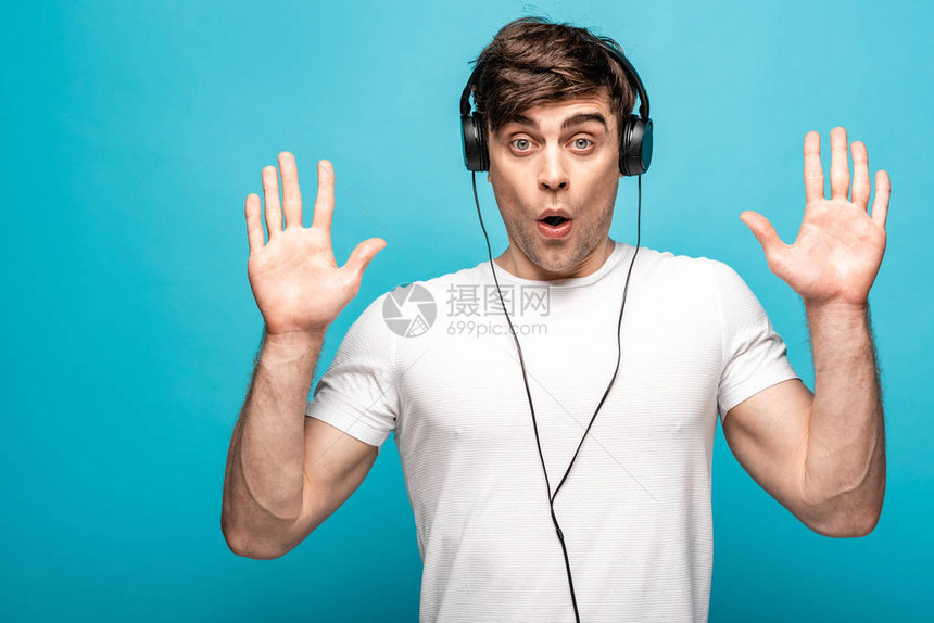 沮丧的年轻男子在蓝色背景下听耳机音乐时放弃手势图片