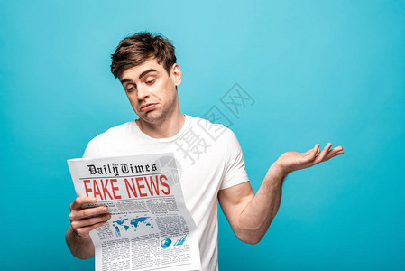 沮丧的青年男子在阅读蓝色背景假新闻报纸时图片