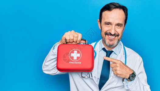 中年英俊的医生穿着外套和听诊器拿着急救箱微笑着用手和图片