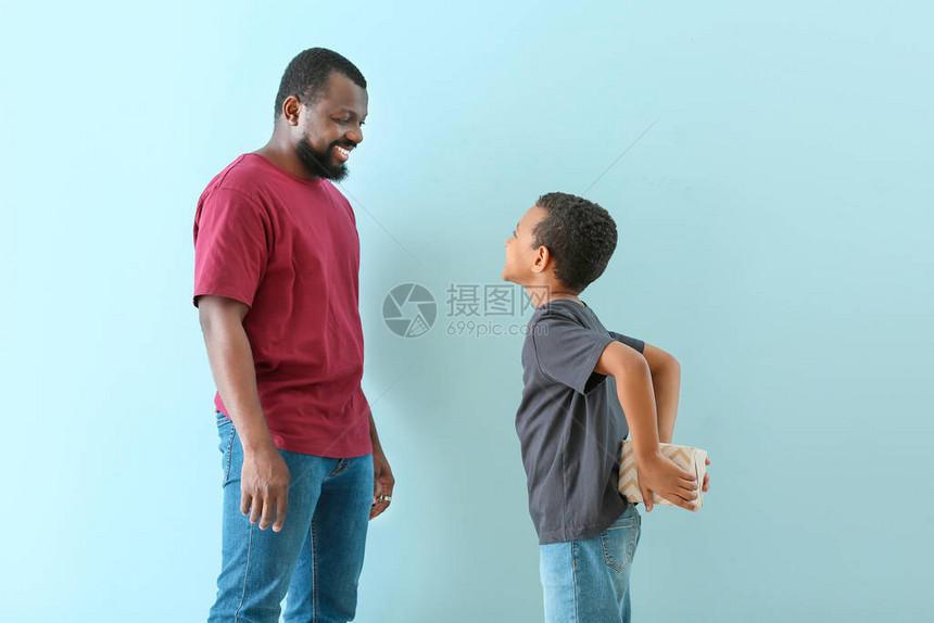 非裔美国小男孩背着他父亲的彩色背景躲在背后图片