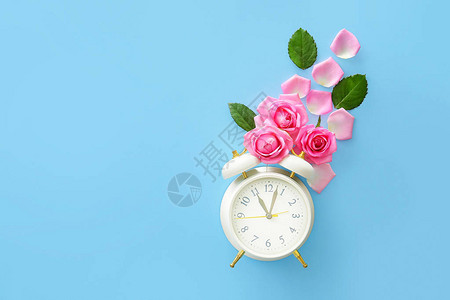 美丽的玫瑰花朵与彩色背景上的闹钟图片