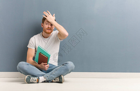坐在地板上坐着的年轻红发学生男子图片