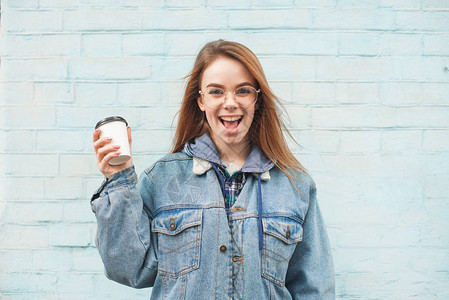一个快乐有魅力的女孩手里拿着一杯咖啡的肖像站在蓝色墙壁的背景上图片