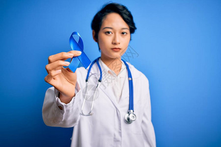 戴着听诊器和外套的年轻漂亮亚洲医生女孩拿着蓝色癌症丝带图片