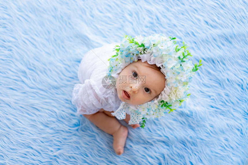 一个美丽的小女孩坐在蓝色毛地毯上戴着一顶由鲜花制成的图片