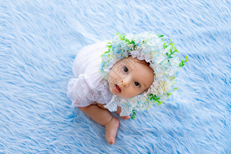 一个美丽的小女孩坐在蓝色毛地毯上戴着一顶由鲜花制成的背景图片