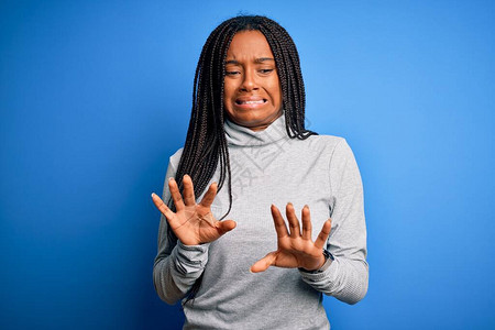 年轻的非洲裔美国妇女穿着休闲高领毛衣站在蓝色孤立的背景上厌恶的表情图片