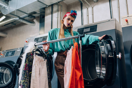 头巾的年轻时尚女站在现代自助洗衣店的衣架图片