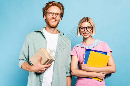 戴眼镜的青年学生在蓝色上站立时持有图片