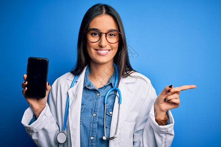 身戴眼镜和大衣手持智能手机的年轻美丽的黑头发女医生图片