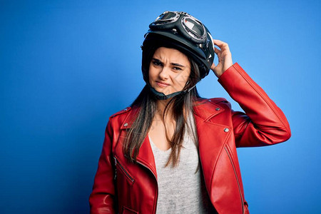 戴着摩托车头盔和夹克的年轻美丽的黑发摩托车手女人对问题感到困惑和好奇图片