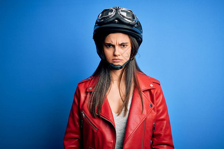 年轻漂亮的黑发摩托车手女人戴着摩托车头盔和夹克怀疑和紧张图片