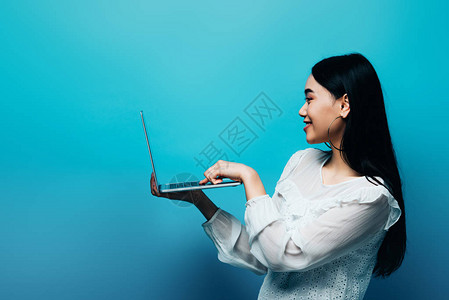 身穿白色衬衫手持蓝色背景笔记本电脑的亚洲女图片
