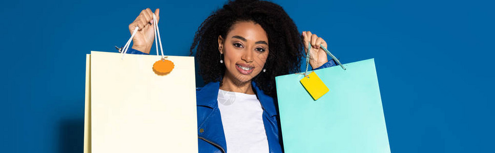 微笑的美丽非洲裔美国女人拿着蓝色背景的购物图片