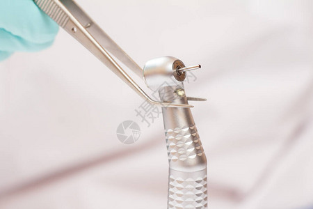 特写牙医的手在乳胶手套与镊子和高速牙科手机在模糊的背景医疗工具图片