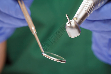特写牙医的手在乳胶手套与口镜和高速牙科手机在模糊的背景医疗工具图片