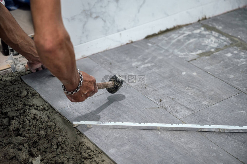 铺瓦工的手和用木槌敲打地板上的花岗岩瓷砖图片