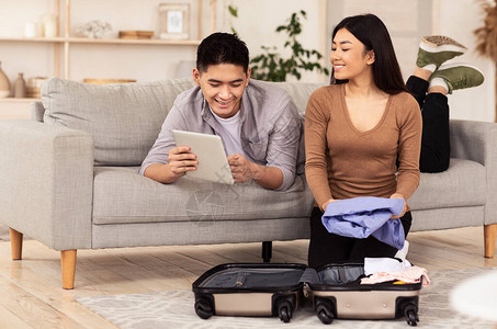 在家随西装行李坐家旅行时使用平板电脑包装的快乐夫妇家背景图片