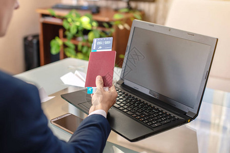 男子商人持有机票和护照在互联网上使用笔记本电脑购买在线购图片