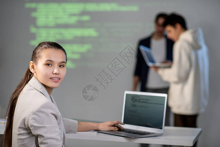 聪明的年轻学生坐在笔记本电脑前的办公桌边看着你图片