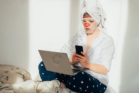 年轻女子在自我隔离期间使用笔记本电脑和手机在家和床上工作图片