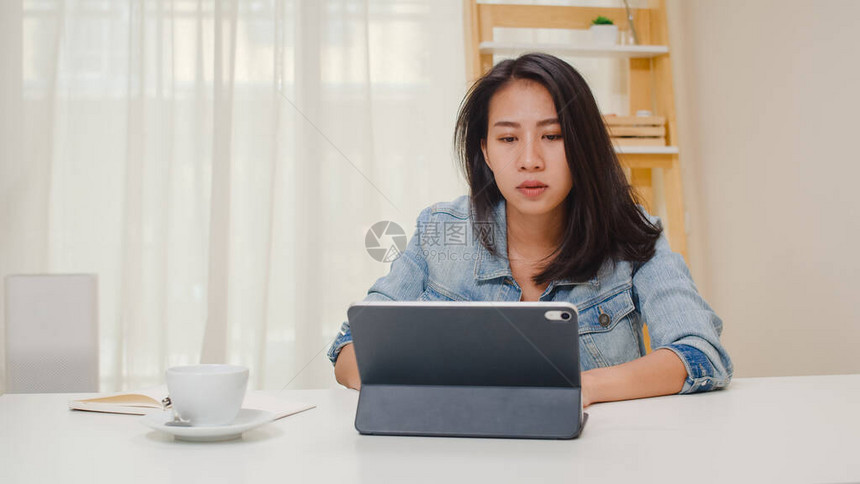 沮丧的亚洲年轻女士在办公桌上无法使用平板电脑时遇到了问题使用平板电脑在家庭办公室客厅工作的自由职业智能商图片