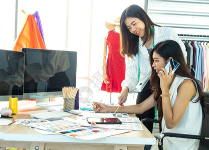 两位亚洲女设计师正在打电话咨询客户关于女装设计的问题从目录中确图片