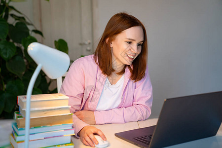 一位身穿粉色衬衫的深色头发的女士正在家里的办公桌前工作或学习图片