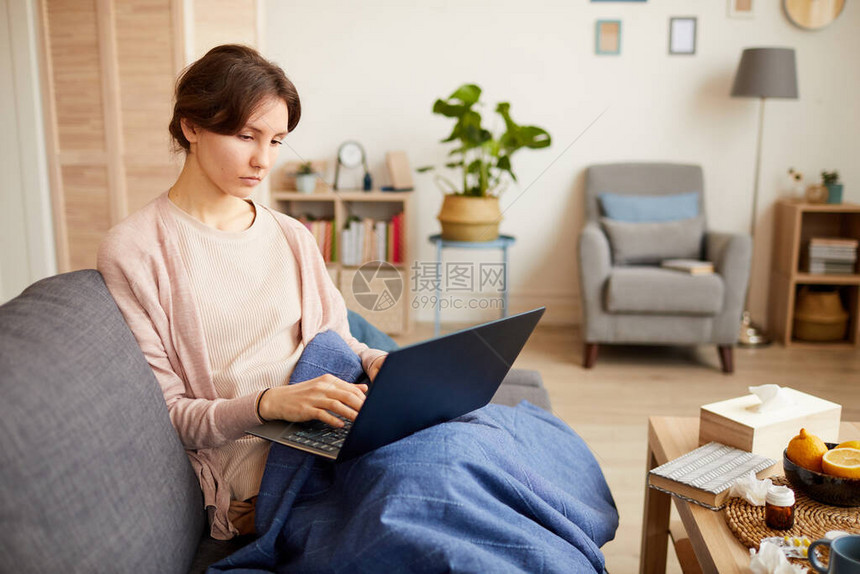 坐在沙发上和打笔记本电脑上的年轻妇女因大流行病而留在家中图片