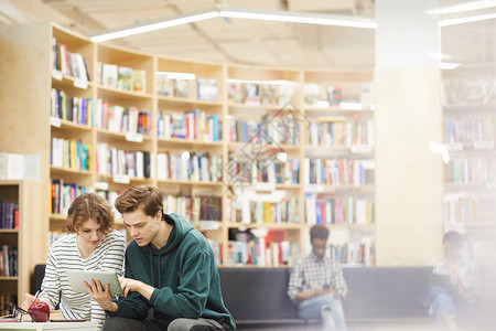 穿着休闲装的严肃集中的年轻学生坐在现代图书馆区背景图片