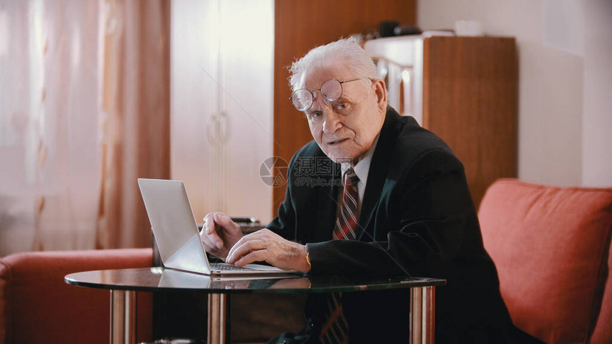 一个戴眼镜的老人坐在笔记本电脑旁边看着摄图片
