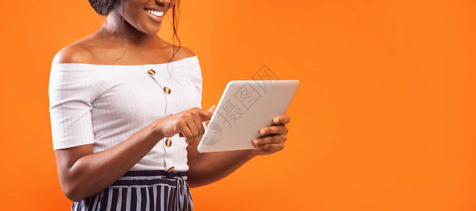在橙色工作室背景上站立的无法辨认的利用平板电脑的非洲女孩图片