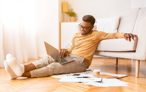 黑人学生家伙使用笔记本电脑学习喝咖啡坐在家里的地板上图片