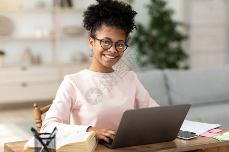 在笔记本电脑上的黑人女孩在网上对坐在家桌边的摄像机微笑图片