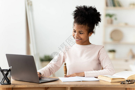 非洲女青少年在家办公桌旁在线进行笔记本电脑研究做家庭工作图片