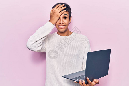 持有笔记本电脑的非洲青年美国人用手顶着头惊讶和愤怒的脸图片