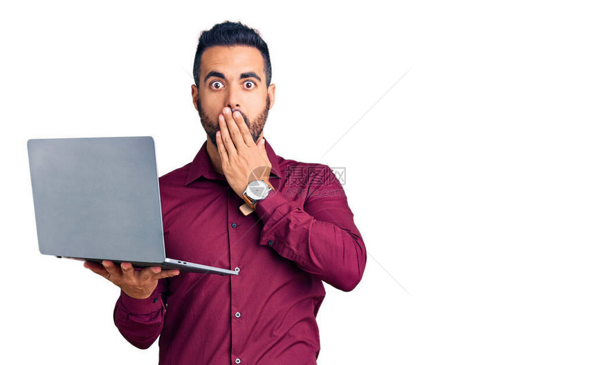 带着笔记本电脑亲手遮住嘴部震惊和害怕错误的年轻西班牙男子图片