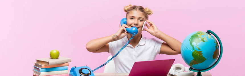 在笔记本电脑附近用电话和智能手机交谈的女学生以及被粉红图片
