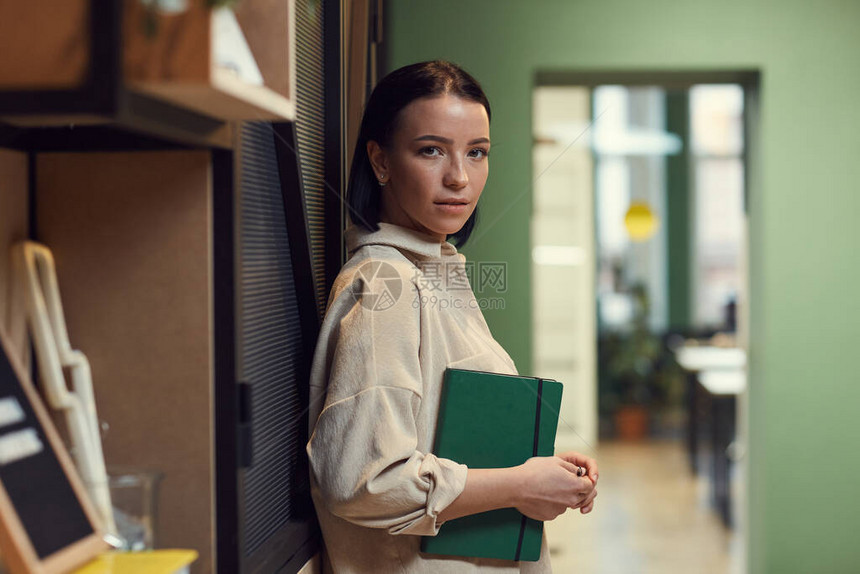 年轻商业女青年在办公室站着时持笔记纸和图片